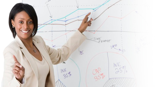 Woman smiling whilst pointing to graphs on a whiteboard